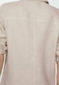 Camicia in lino beige con una vestibilità semplice e rilassata. Tessuto leggero, maniche arrotolate e dettagli sul retro. Design minimalista senza decorazioni.