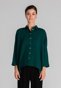 Camicia verde acqua con colletto, vestibilità ampia e maniche a tre quarti. Tessuto morbido con una consistenza liscia e orlo curvo.