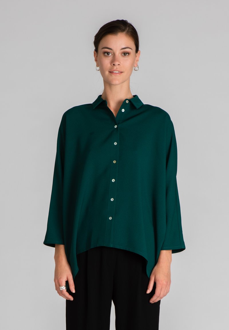 Camicia verde acqua con colletto, vestibilità ampia e maniche a tre quarti. Tessuto morbido con una consistenza liscia e orlo curvo.