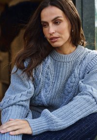 Hellgrauer gestrickter Pullover mit Zopfmuster und gerippten Bündchen. Weiche Textur mit Rundhalsausschnitt und weiten Ärmeln.