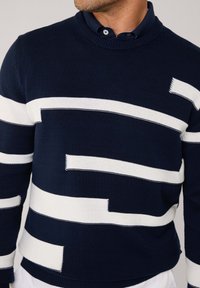 Maglione a maglia blu navy con strisce orizzontali bianche di larghezze variabili, scollo rotondo, tessuto testurizzato e polsini e bordo a coste.
