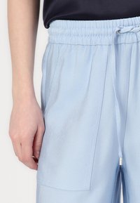 Pantalones de color azul claro con cinturilla elástica y cordón. Presentan una tela texturizada con patrón y bolsillos laterales.