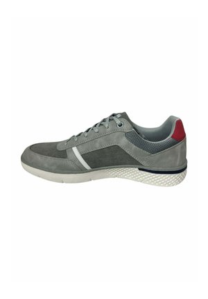 Zapatilla deportiva gris y gris oscuro con cordones, suela blanca, talón texturizado, franja blanca lateral y detalle rojo en la parte trasera.