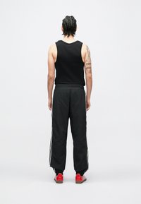 Fekete ujjatlan felső és fekete melegítőnadrág fehér oldalsávval. Piros tornacipő egészíti ki a megjelenést. Az anyag sima és könnyűnek tűnik.