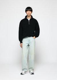 Svart, stripete strikket hettegenser med halv-glidelås i kragen, kombinert med lyse, løstsittende jeans og hvite joggesko.