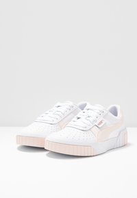 Vita sneakers med rosa accenter, med en texturerad tå, perforerat ovandel och en kontrasterande texturerad sula. Inkluderar snören och varumärkeslogotyp.