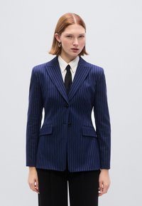 Μπλέιζερ σε σκούρο μπλε απόχρωση με λεπτές ρίγες, εφαρμοστή γραμμή, δύο εμπρόσθιες τσέπες, γιακάδες με εγκοπή, κλείσιμο με ένα κουμπί και απαλό ύφασμα.