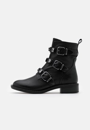 Bottine noire en cuir avec trois boucles décoratives ornées de strass, petit talon, bout arrondi et languette d'extraction à l'arrière.