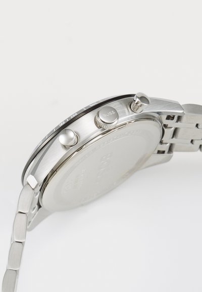 Montre en acier inoxydable avec une lunette noire, deux poussoirs et une couronne texturée. Dotée d'un bracelet à maillons et d'un dos lisse avec des lettres en relief.