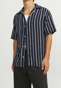 Granatowo-biała, w paski, koszula z krótkim rękawem, z kołnierzykiem, zapinana na guziki i w strukturze materiału. Nosi się ją na białej bluzce na ramiączkach.