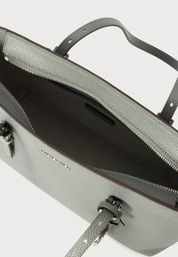 Sac en cuir gris clair avec surface texturée, fermeture éclair et deux poignées. L'intérieur est sombre avec une étiquette de marque discrète.