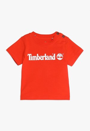 Camiseta roja de manga corta para bebé con el logo blanco de Timberland y gráfico de árbol, con dos botones a presión negros en el hombro izquierdo.