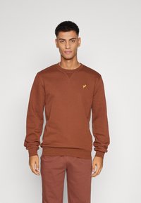 Brun sweatshirts med rund hals, lange ærmer og ribbede manchetter. Har et lille gult logo på brystet. Glat stofstruktur.