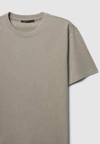 T-shirt a manica corta color beige chiaro con tessuto testurizzato. Presenta un colletto a coste e un design pulito e semplice senza motivi.