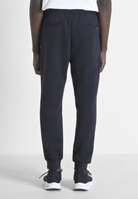 Marineblauwe joggers met een elastische tailleband, zijzakken en taps toelopende cuffs. Gemaakt van een zachte, gladde stof met een ontspannen pasvorm.