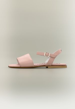 Sandale plate rose avec bout ouvert, bride à la cheville avec boucle argentée, et semelle beige, vue de profil sur un fond neutre.