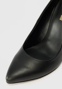 Pantofii cu toc înalt din piele neagră au un vârf ascuțit și o textură netedă. Acest model are un design curat și clasic, cu un profil elegant.