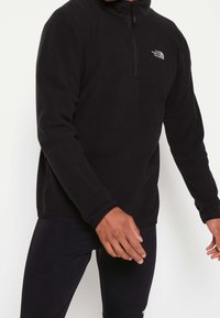 Pullover in pile nero con colletto a mezzo zip, dotato di maniche lunghe e logo ricamato sul lato sinistro del petto. Tessuto liscio, vestibilità regolare.