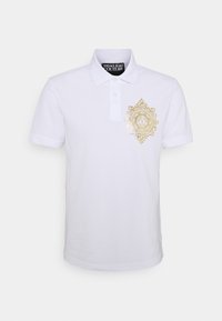 Weißes Polo-Shirt aus Baumwolle mit einem goldenen dekorativen Emblem auf der linken Brust, ausgestattet mit einer Dreiknopf-Leiste und kurzen Ärmeln.