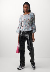 Blusa a righe blu e bianche con stampa floreale, maniche a palloncino e design smock. Abbinata a pantaloni neri lucidi e una piccola borsa rosa.