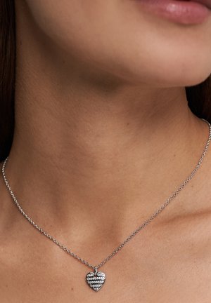 Silberne Halskette mit Herzanhänger, der abwechselnd Reihen aus klaren Steinen und glattem Metall zeigt. Die Kette ist zart und rund.