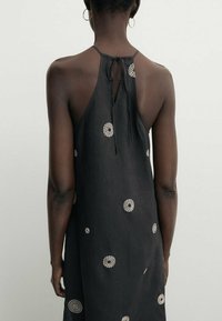 Robe en lin noir avec un col halter et un lien dans le dos. Présente des points de broderie blancs circulaires partout. Texture lisse, longueur cheville.