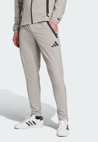 Pantalones deportivos grises con un ajuste slim, que cuentan con bolsillos con cremallera negros y un logo negro. Están fabricados con material suave y ligero.