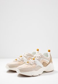 Beige och vita sneakers med texturerad stickad ovandel, suéde-accenter och orange detaljer. Rund tå, vadderad sula och snörning.