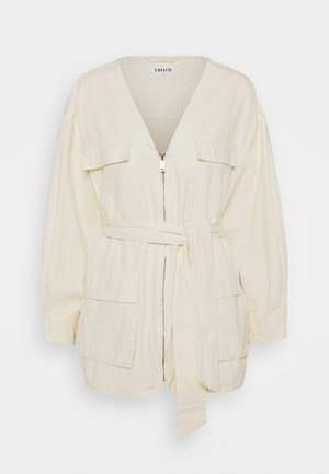 Veste en coton crème avec des manches longues, un col en V, fermeture éclair à l'avant, deux poches plaquées et une taille nouée. Texture lisse, coupe décontractée.