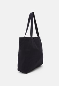 Sac fourre-tout en toile bleu marine avec de longues sangles plates pour l'épaule et un design simple et non structuré. Sans quincaillerie ni motifs visibles.