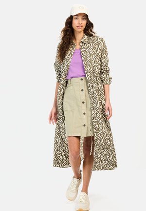 Lange mouwen, dierenprint shirt in olijfgroen en beige, gecombineerd met een lavendeltop en een beige rok met knopen, afgemaakt met witte sneakers.