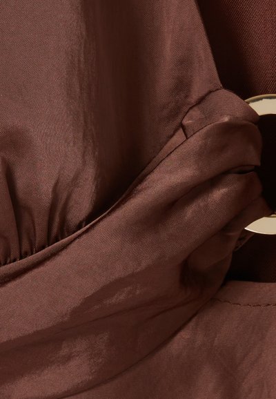 Tissu satin marron avec une texture lisse, présentant des détails froncés et un accent circulaire doré.