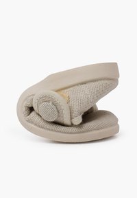 Zapato plegable en beige claro con upper de tela texturizada y suela de goma lisa. Presenta una forma redondeada y un diseño minimalista con un acento de botón.