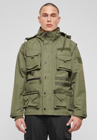 Zelena uporabna jakna z več sprednjimi žepi, nastavljivo kapuco in detajli z zadrgo. Izdelana iz trpežnega blaga z matiranim zaključkom.