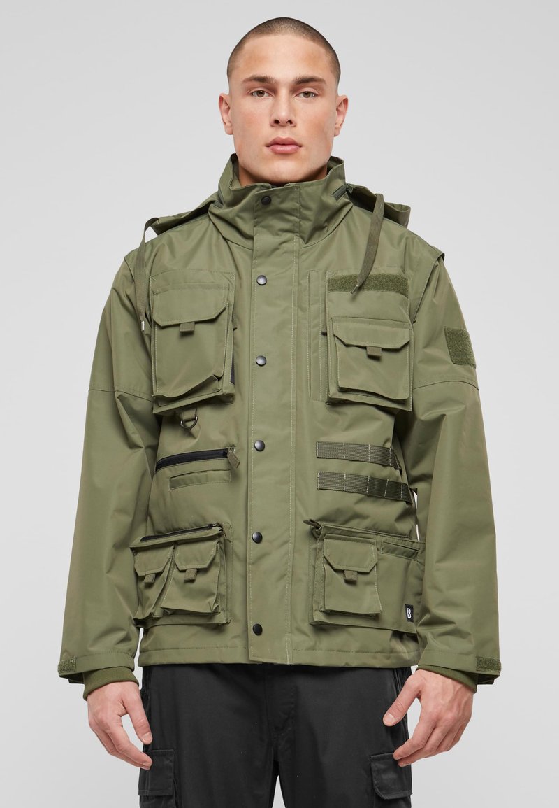 Zelena uporabna jakna z več sprednjimi žepi, nastavljivo kapuco in detajli z zadrgo. Izdelana iz trpežnega blaga z matiranim zaključkom.