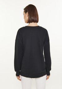 Svart långärmad sweatshirt med avslappnad passform, ribbad rund halsringning och cuffs, med en mjuk textur och rundad nederkant.