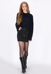 Granatowy sweter dzianinowy o luźnym kroju, noszony z czarną spódnicą dżinsową. Modelka ma na sobie półprzezroczyste czarne rajstopy i czarne kozaki do kolan z klamrami.