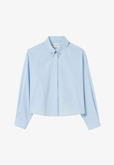 Camisa cortada de color azul claro con mangas largas, cuello abotonado y dos botones decorativos en la parte frontal, hecha de una tela suave.