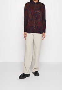 Långärmad skjorta med paisleymönster i mörka toner, knäppning fram, parat med beige vida byxor och svarta platåskor.