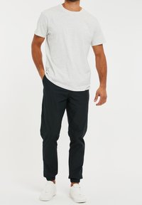 Lichtgrijs T-shirt met korte mouwen en ronde hals, gecombineerd met zwarte taps toelopende broek en witte sneakers. Glad materiaal met minimale details.