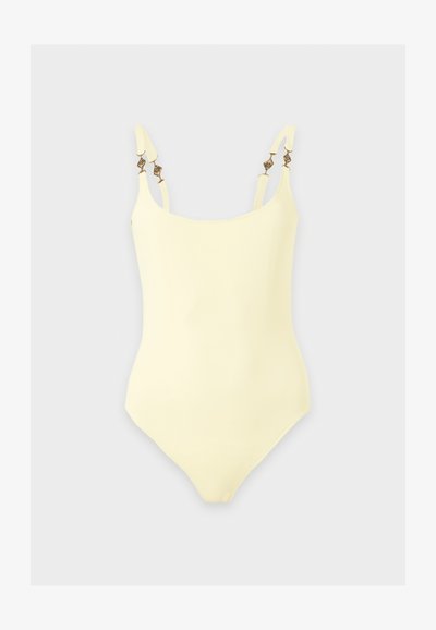 Maillot de bain une pièce jaune avec fines bretelles ajustables décorées de perles métalliques sur un fond gris clair.