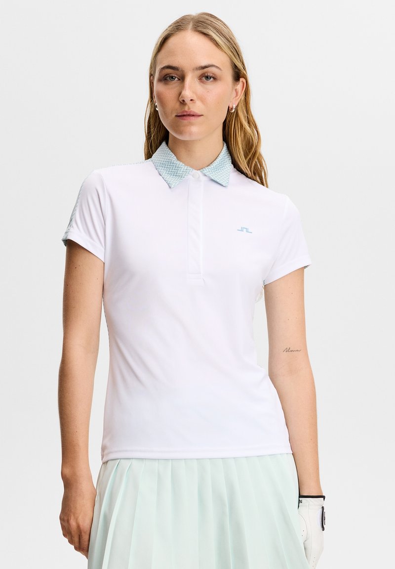 Polo blanc avec un col à motif bleu clair, manches courtes et logo discret sur la poitrine. Tissu lisse et léger.