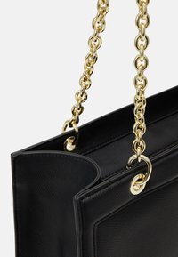 Bolso de mano de cuero negro con un acabado texturizado, que cuenta con una larga correa de cadena dorada y acentos metálicos dorados en los laterales.