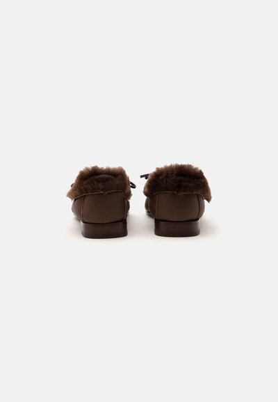 Paire de mocassins en cuir marron avec une doublure en fourrure duveteuse visible de dos, sur un fond clair uni.