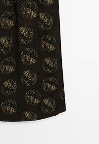 Sort stof med store runde, teksturerede mønstre i guld. Designet ligner garnkugler med krydsmønster. Glat tekstur.