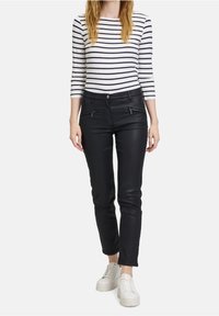 Černé úzké kalhoty se dvěma zipovými předními kapsami, doplněné bílou a námořnickou pruhovanou dlouhým rukávem. Bílé tenisky dotvářejí celý outfit.