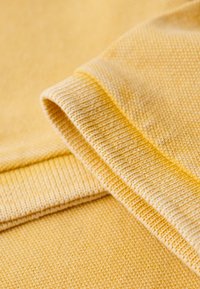 Tessuto a maglia giallo con una superficie testurizzata e bordi a coste. I strati piegati mostrano motivi variabili e cuciture lisce.
