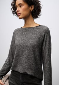 Maglione grigio a maniche lunghe con una texture morbida e una vestibilità comoda. Caratterizzato da un ampio scollo e polsini a costine, abbinato a jeans neri.