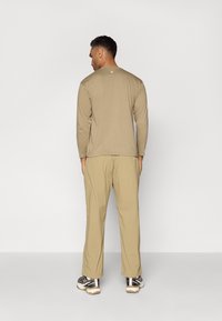 Long-sleeve, light brown shirt with a round neck, paired with beige pants and black and white sneakers. Features minimalist design.