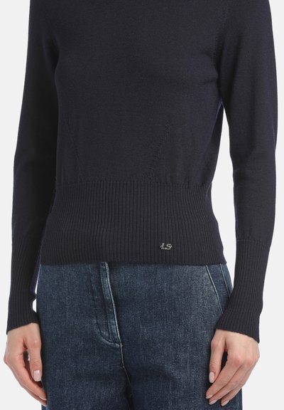 Marineblauer Strickpullover mit gerippten Bündchen und Saum, mit einem Logodetail. Kombiniert mit Jeans, die eine taillierte und strukturierte Optik bieten.